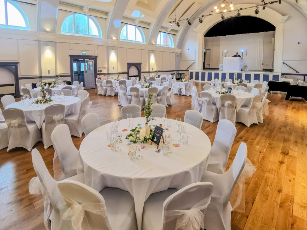 Tables with tablecloths and chairs with chair covers and decorative ribbons set out for wedding